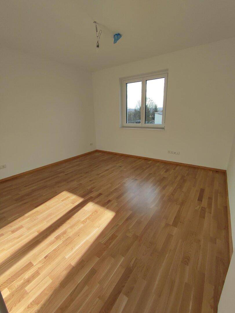 Helles Schlafzimmer mit Holzfußboden und großem Fenster, das viel Tageslicht hereinlässt.