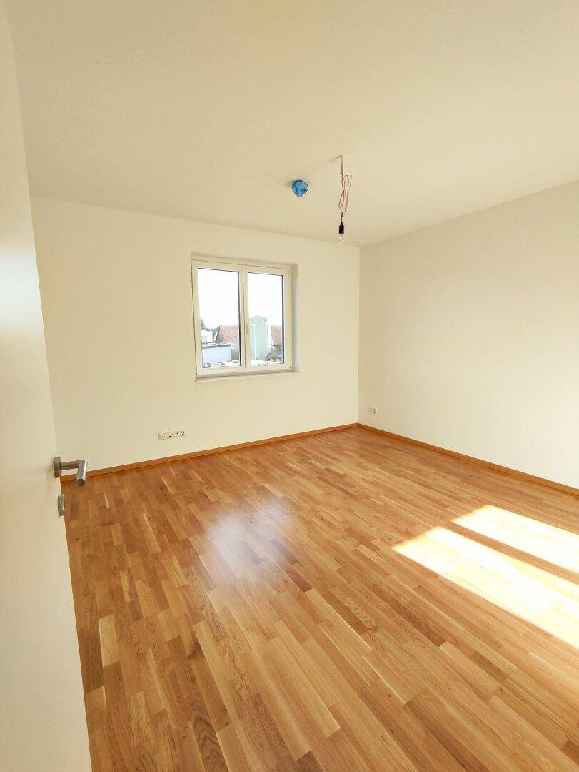 Geräumiges Schlafzimmer mit Parkettboden und Fenster, das einen Blick nach draußen bietet.