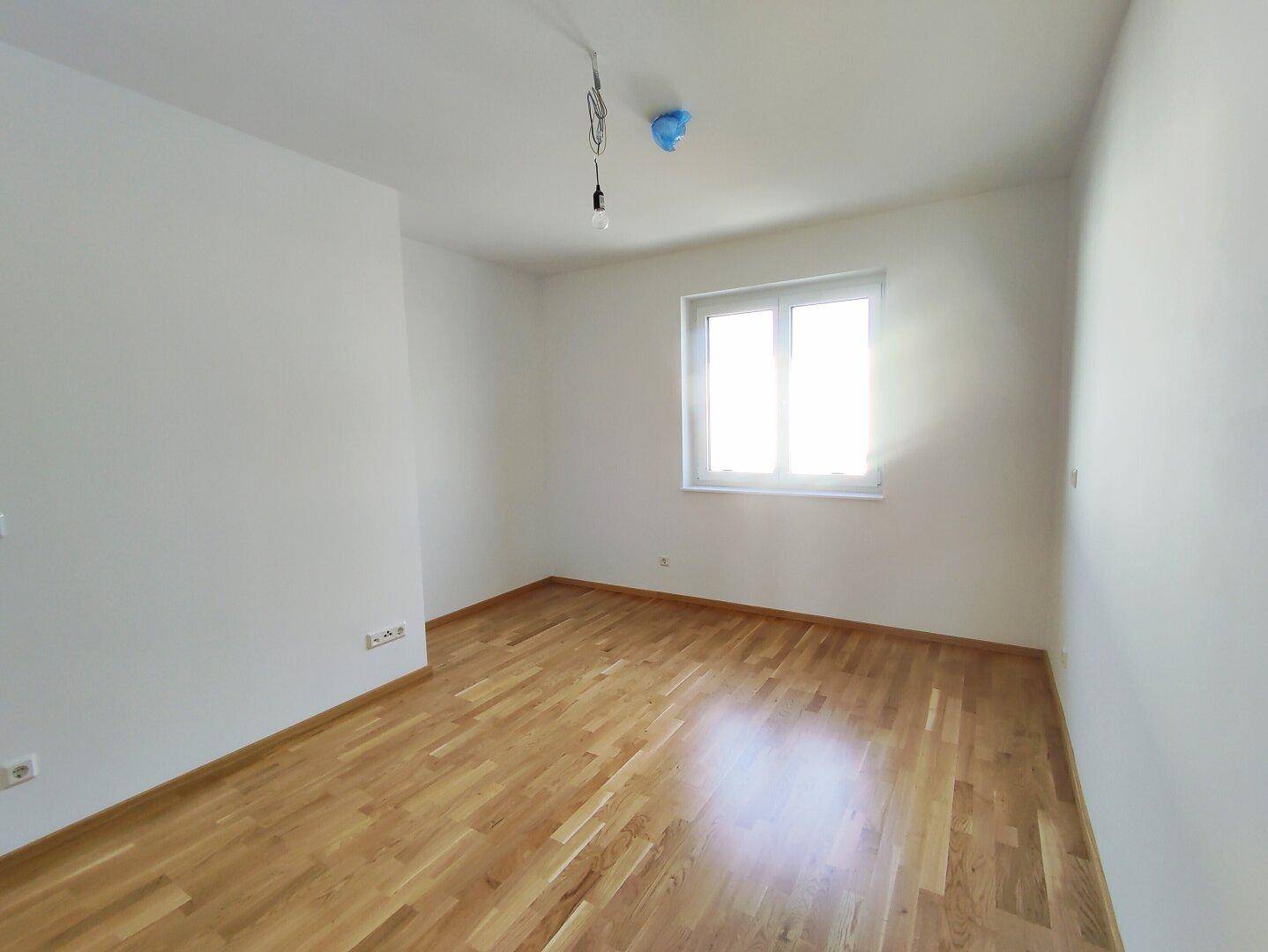 Freundliches Schlafzimmer mit hellem Parkettboden und großem Fenster für optimale Belichtung.