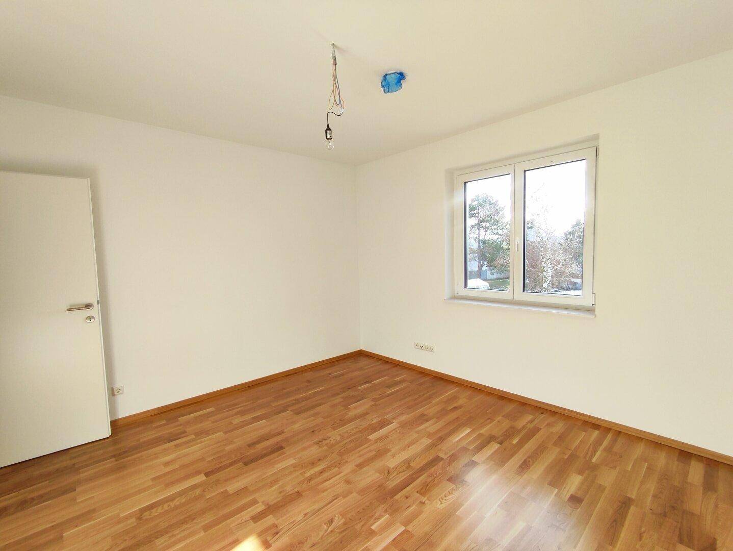 Lichtdurchflutetes Schlafzimmer mit warmem Holzfußboden und weiß gestrichenen Wänden.