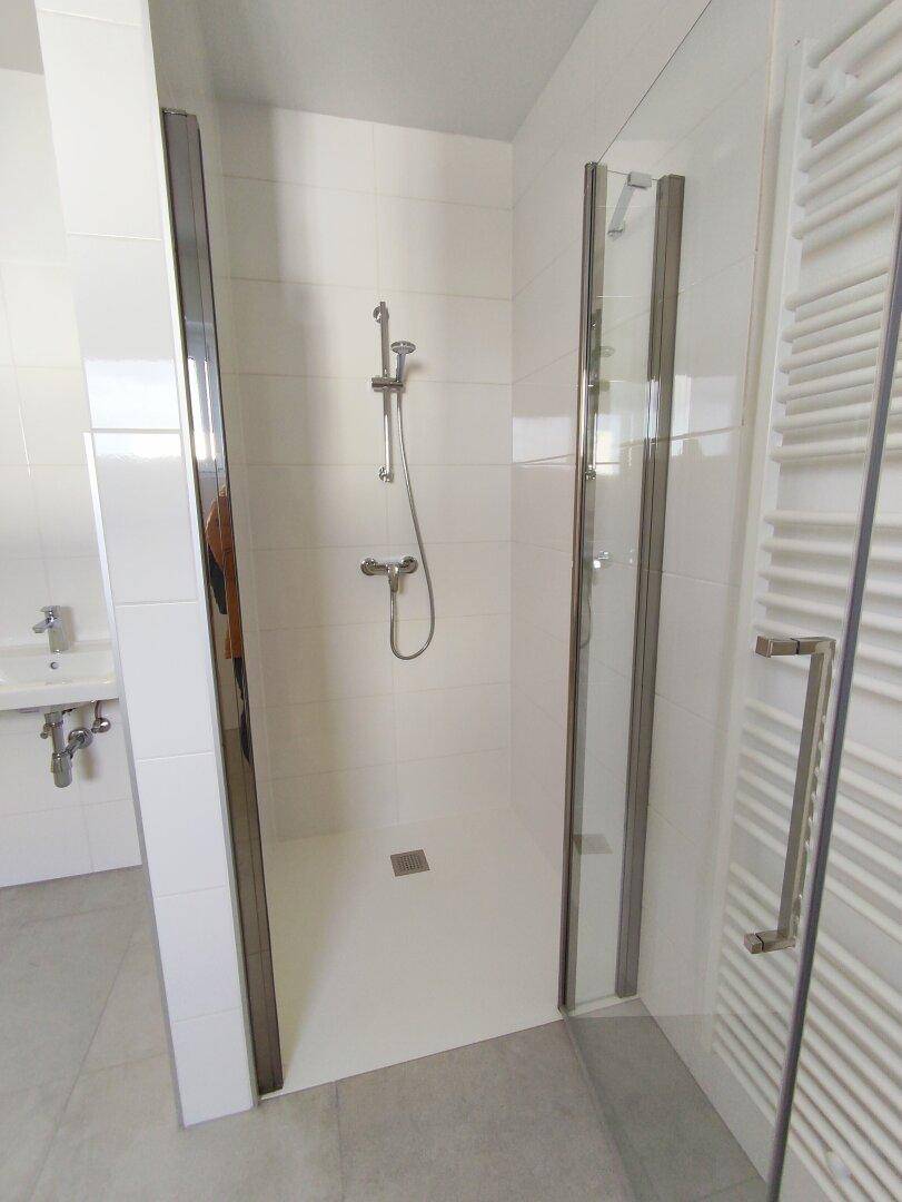 Ebenerdige Dusche mit Glasabtrennung in einem modernen, hell gefliesten Badezimmer.