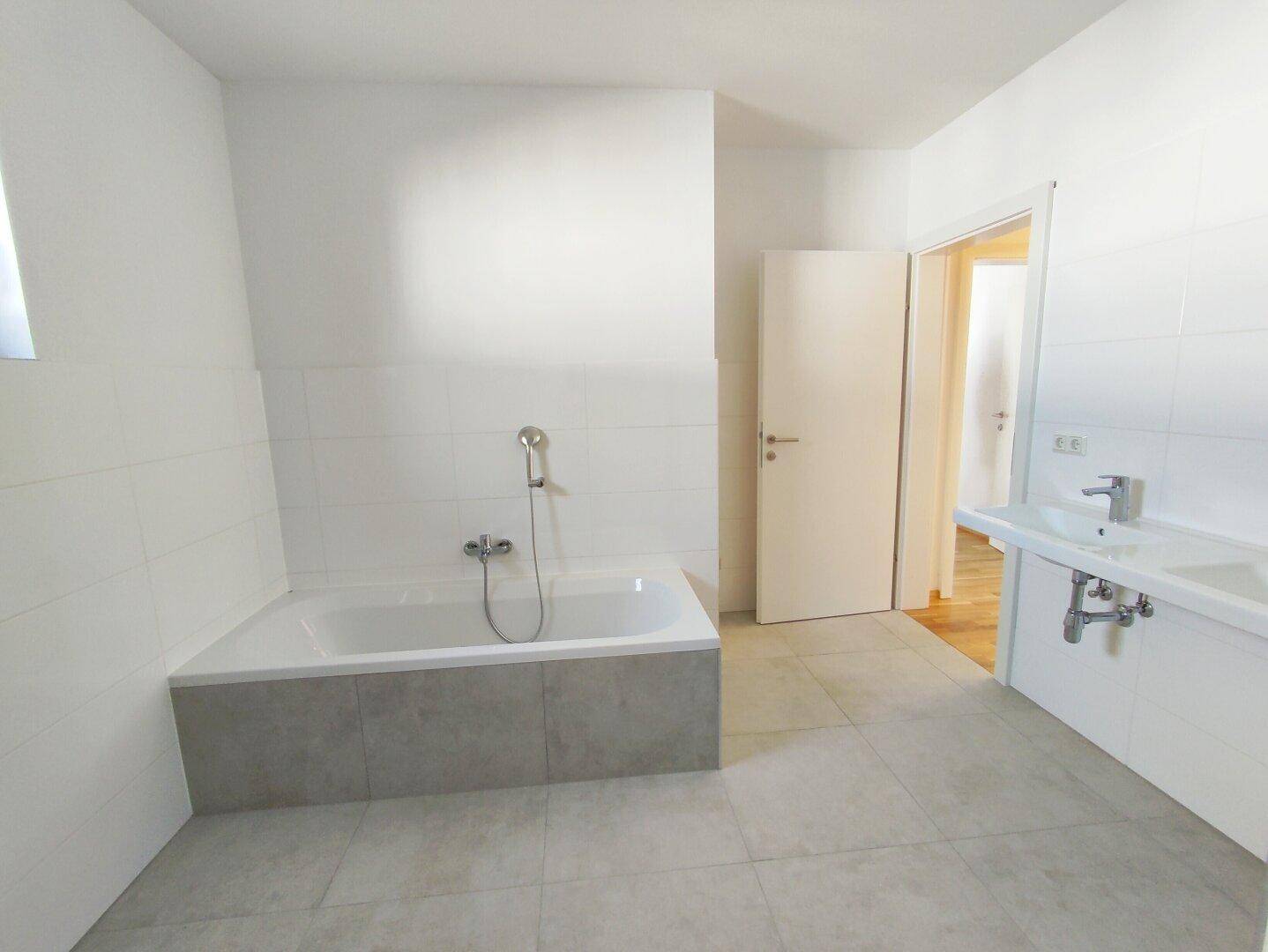 Modernes Badezimmer mit Badewanne, Einzelwaschbecken und hellen Fliesen.