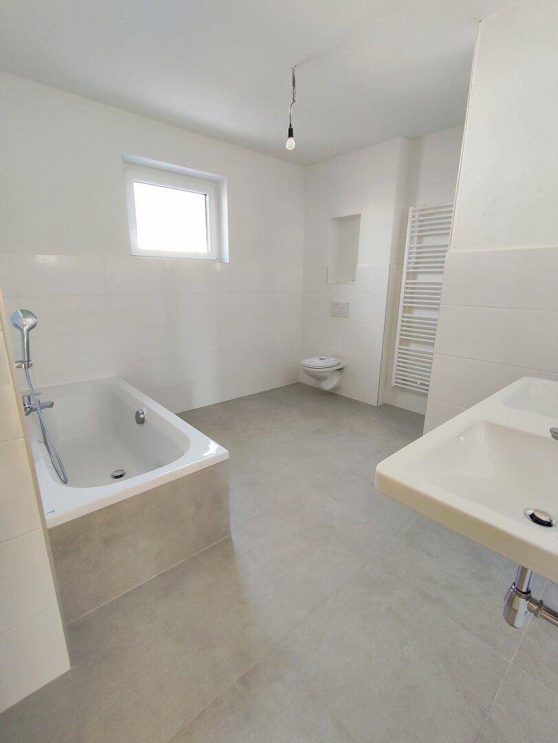 Helles Badezimmer mit Badewanne, Waschbecken, Toilette und Fenster für natürliche Belüftung.