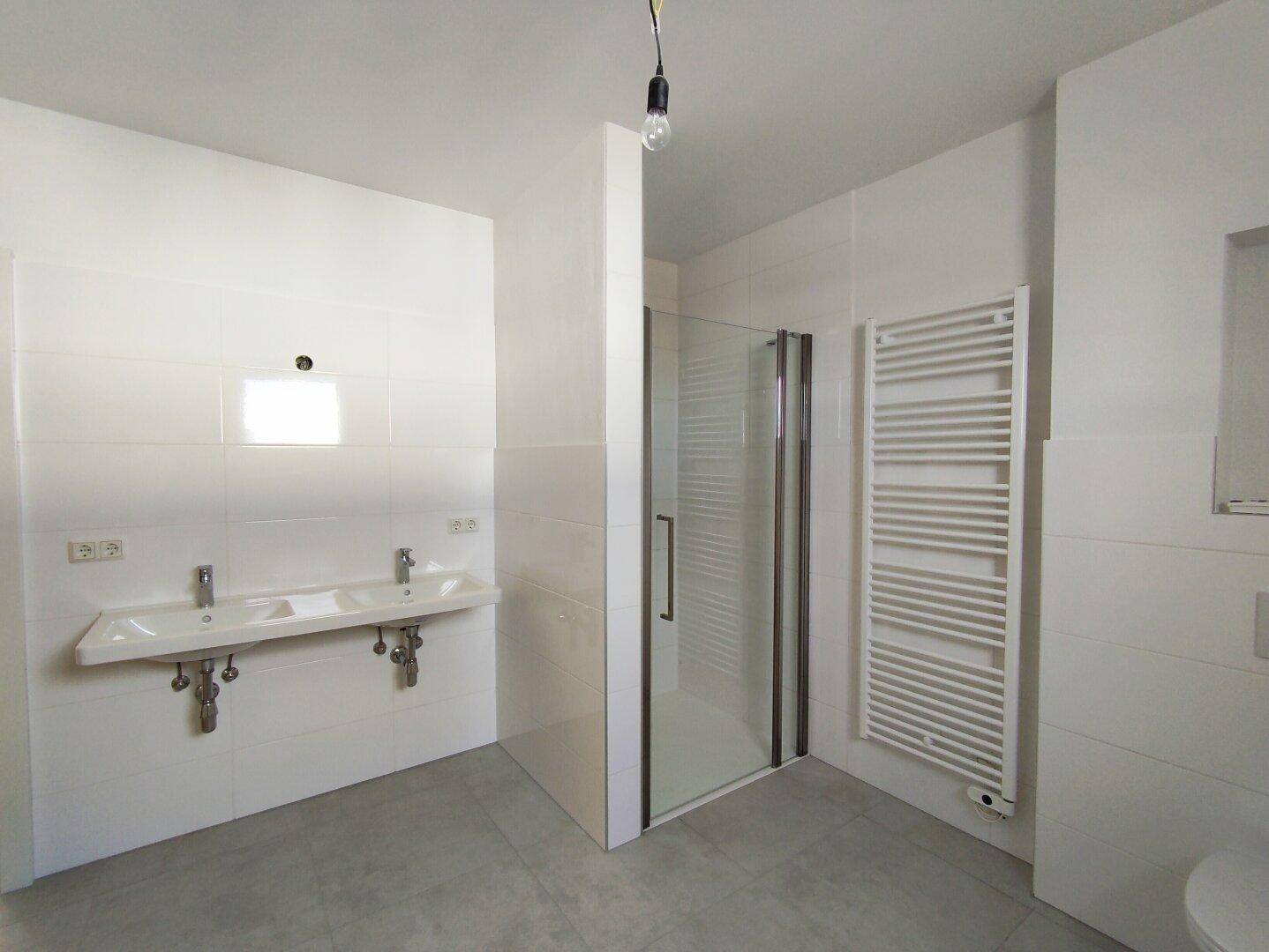 Geräumiges Badezimmer mit Doppelwaschbecken, ebenerdiger Dusche und Handtuchheizkörper.