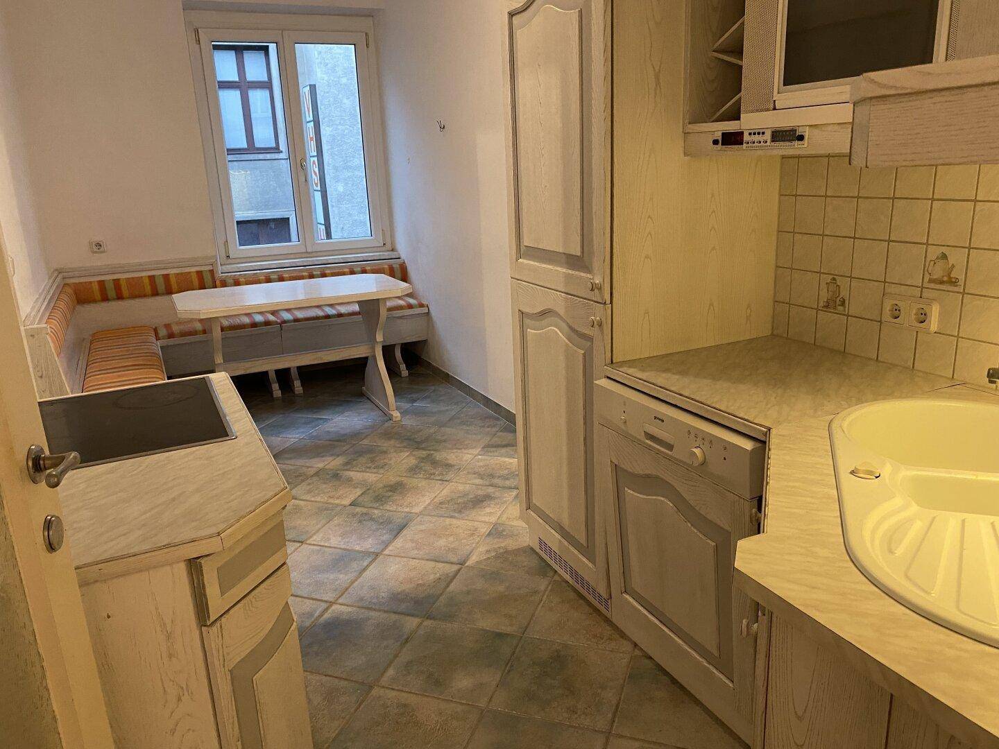 Gemütliche Wohnküche mit Essbereich am Fenster, traditionellen Schränken und Fliesenboden.