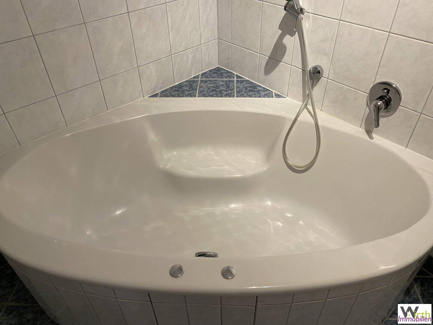 Eckbadewanne mit Duscharmatur und weißen Fliesen in einem Badezimmer.