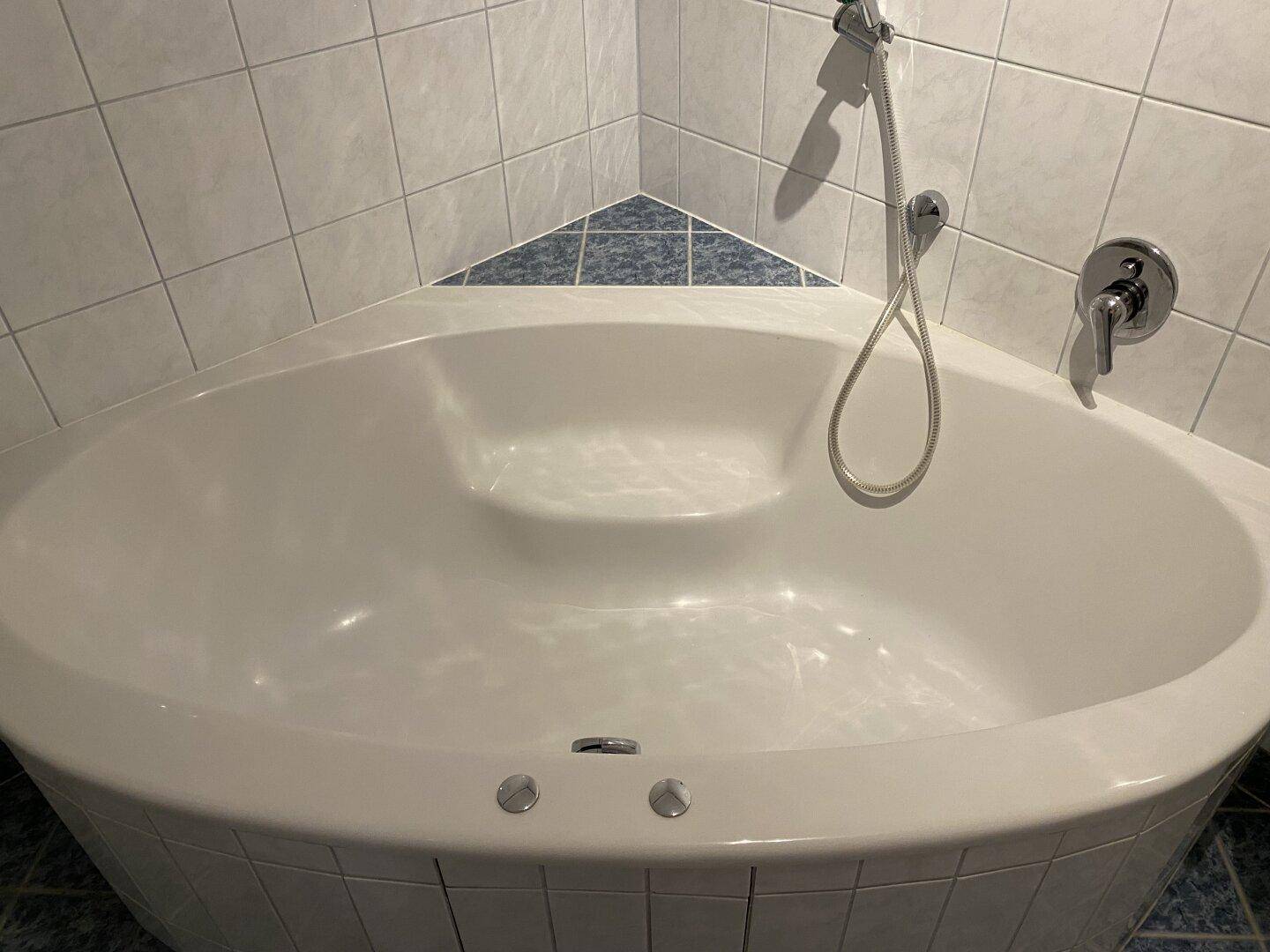 Eckbadewanne mit Duschfunktion und weißen Wandfliesen, akzentuiert durch blaue Bodenfliesen.