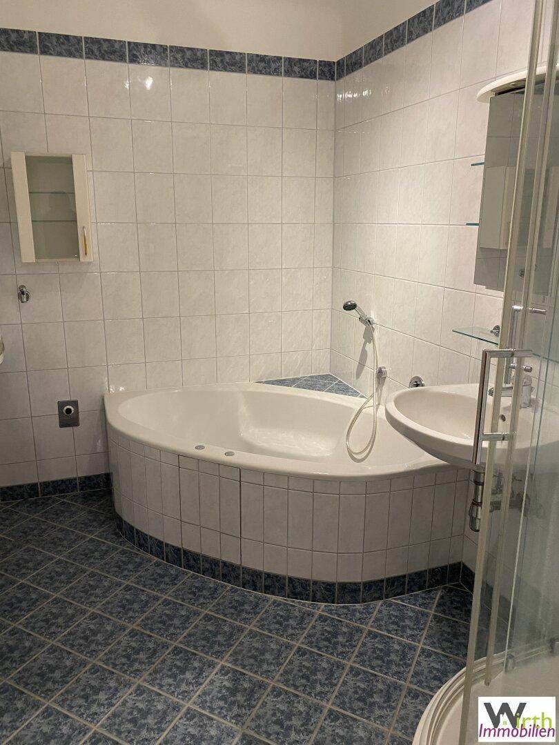 Badezimmer mit Eckbadewanne, Waschbecken und Duschkabine, gefliest in Weiß und Blau.