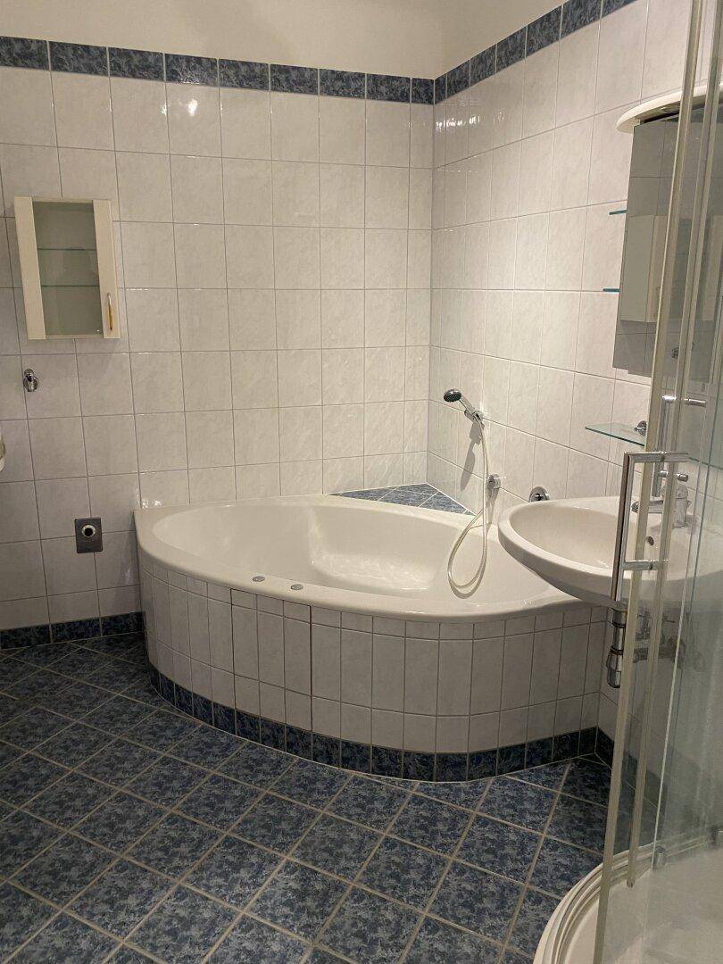 Badezimmer mit Eckbadewanne, Waschbecken und Duschkabine, ausgestattet mit blauen Bodenfliesen.