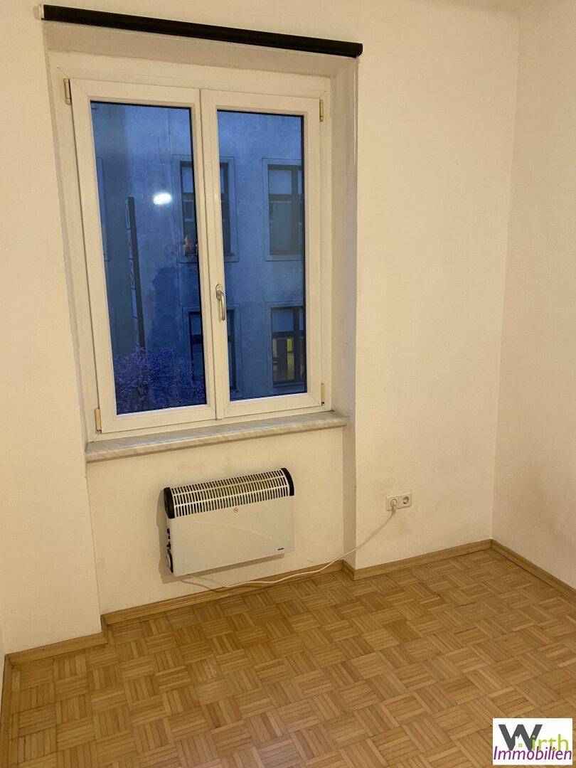 Leerer Raum mit Parkettboden, Fenster und Wandheizkörper.
