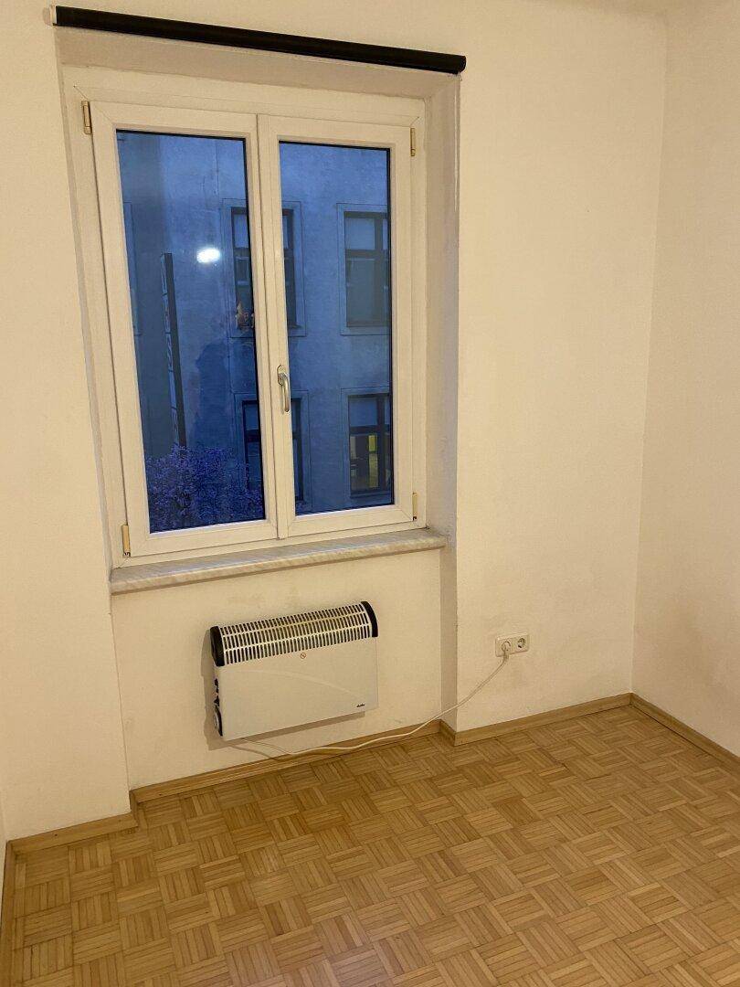 Leerer Raum mit Parkettboden und Fenster, ausgestattet mit einem elektrischen Heizkörper.