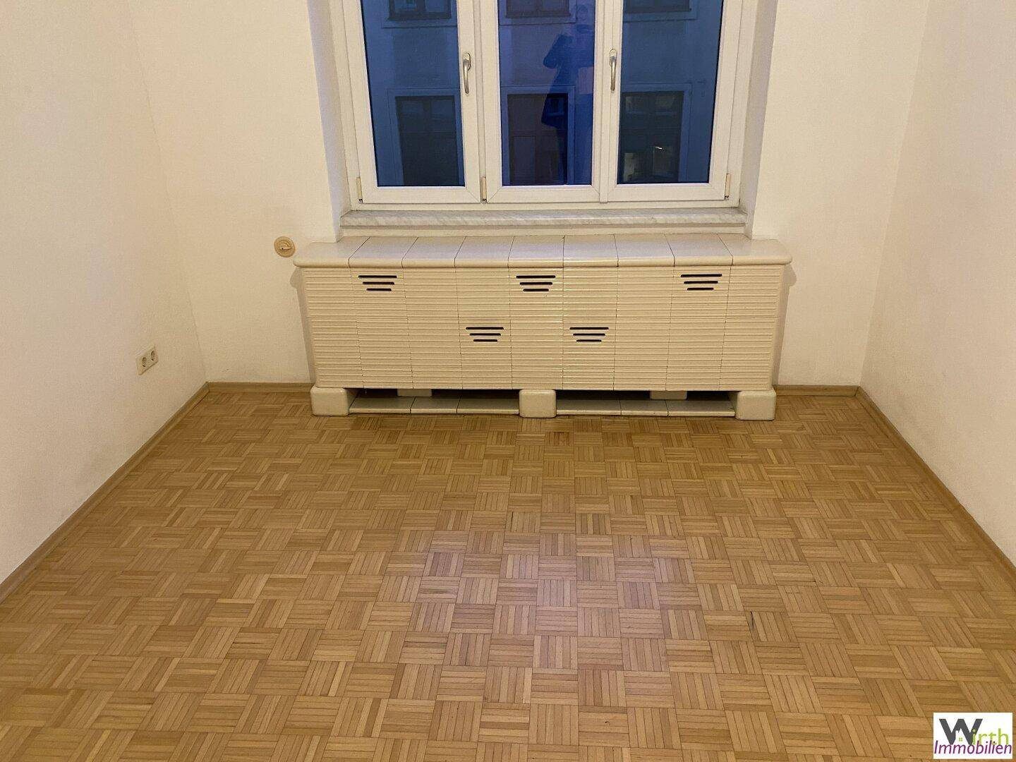 Heller Raum mit Parkettboden und einem Heizkörper unter dem Fenster.