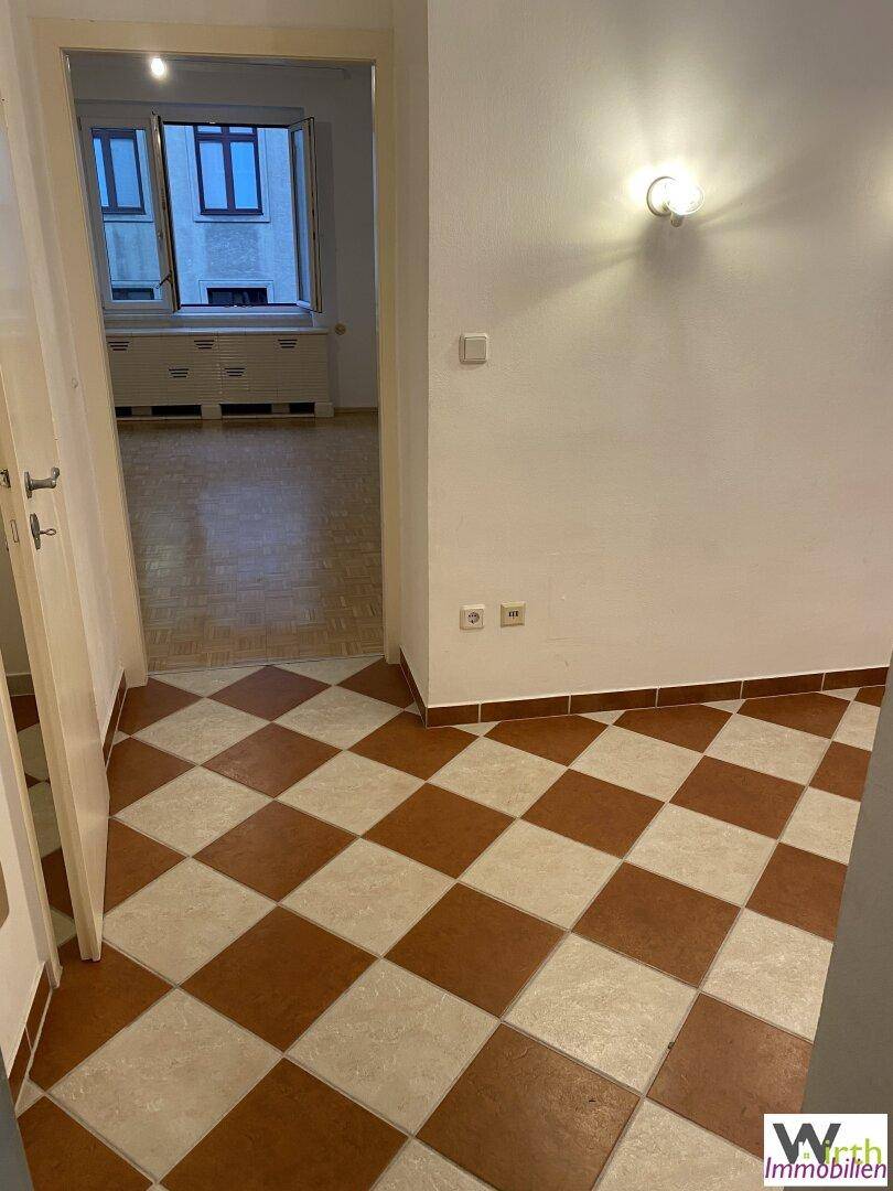 Flur mit Schachbrettmuster-Fliesenboden, der zu einem weiteren Raum führt.