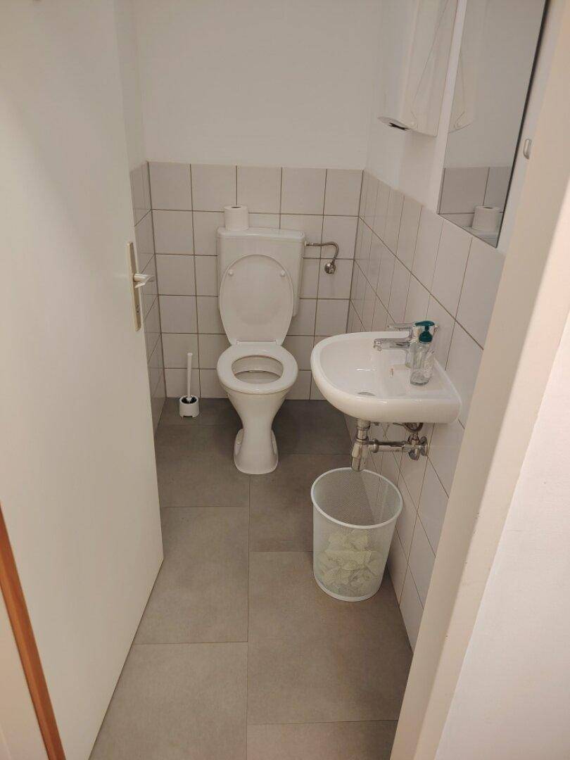 Saubere Toilette mit WC und kleinem Waschbecken, gefliesten Wänden und Boden.