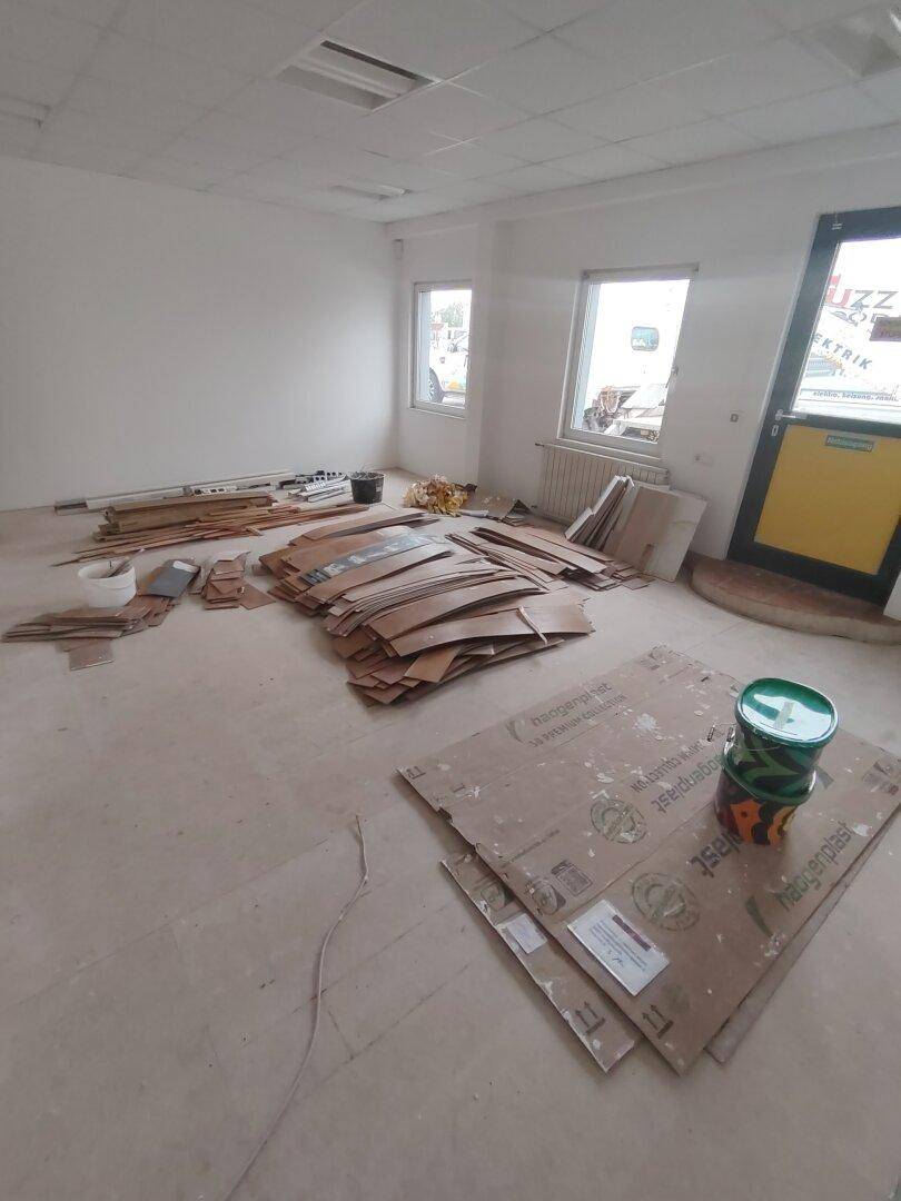 Renovierungsbedürftiger Raum mit Fenstern, Kartons und Baumaterialien auf dem unfertigen Boden.