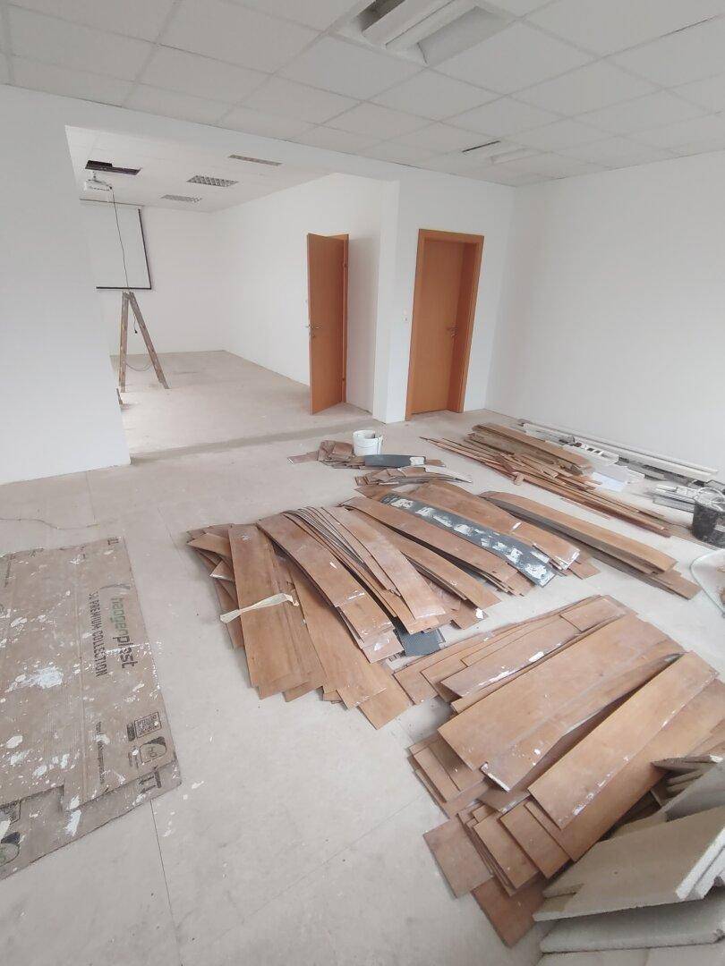 Raum in Renovierung mit Holzbrettern und Kartons auf dem Boden, weiße Wände und Holztüren.