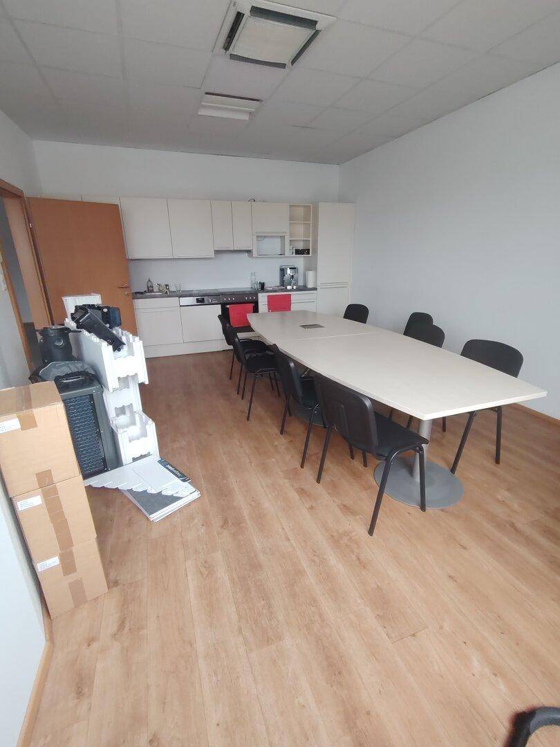 Konferenzraum mit langem Tisch und Stühlen, ergänzt durch eine integrierte Küchenzeile im Hintergrund.