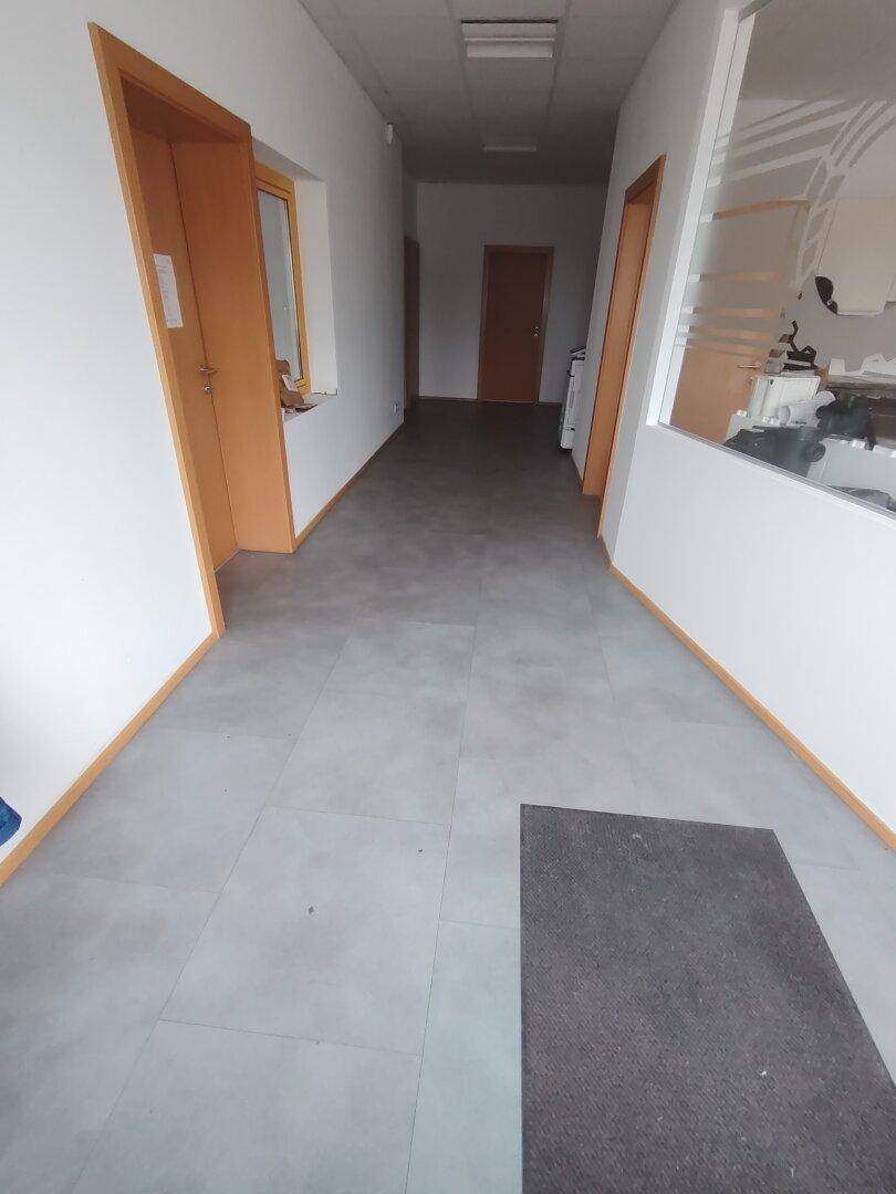 Heller Flur mit grauen Fliesen und weißen Wänden, gesäumt von Holztüren und -rahmen.