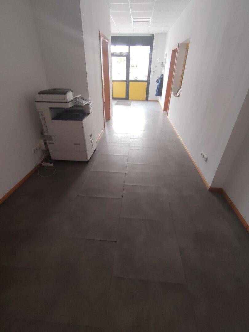 Langer Flur mit Kopierer und einer gelben Tür am Ende, der zu weiteren Räumen führt.