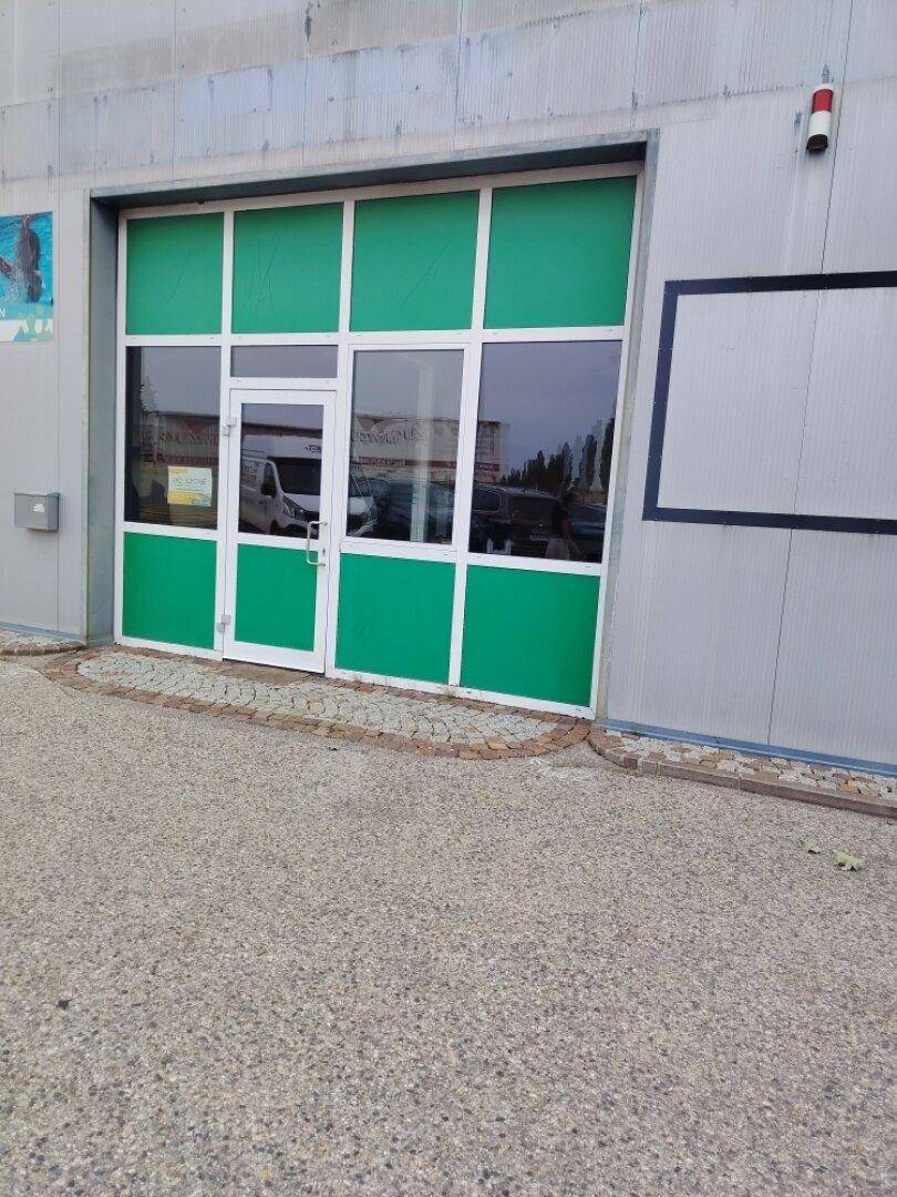 Eingangsbereich eines Gewerbegebäudes mit auffälliger grüner Fensterfront und Tür.