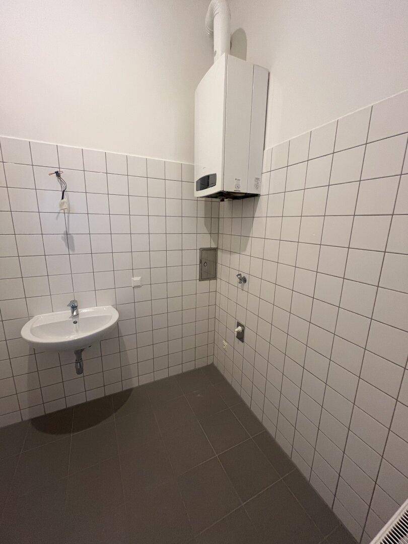 Kleiner Raum mit Waschbecken und Gastherme, gefliest und funktional gestaltet.