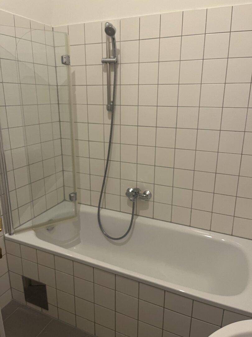 Badezimmer mit Badewanne, Duscharmatur und Fliesen an den Wänden, praktisch und sauber.