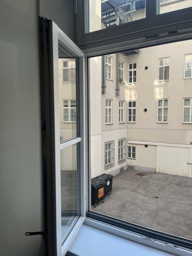 Geöffnetes Fenster mit Blick auf einen ruhigen Innenhof und umliegende Gebäude.