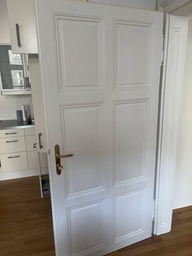 Klassische weiße Tür mit Kassetten und goldfarbenem Griff, passend zum Altbau-Stil.