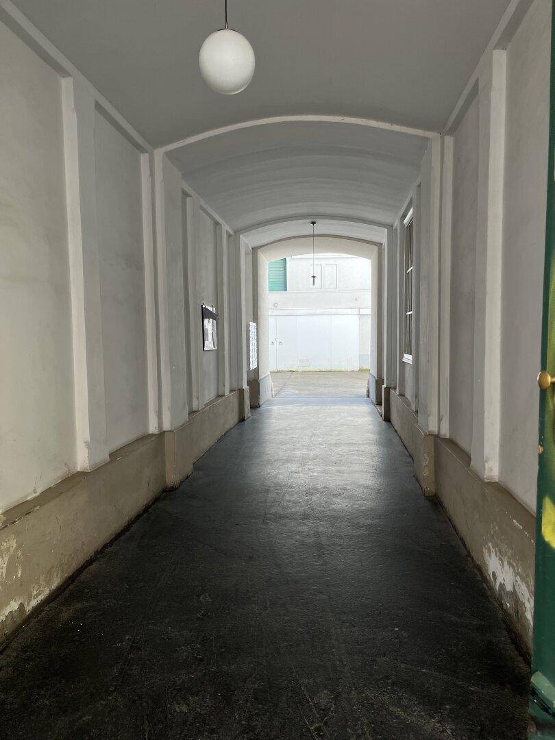 Langer, überdachter Durchgang im Erdgeschoss eines Gebäudes, führt zu einem Innenhof.