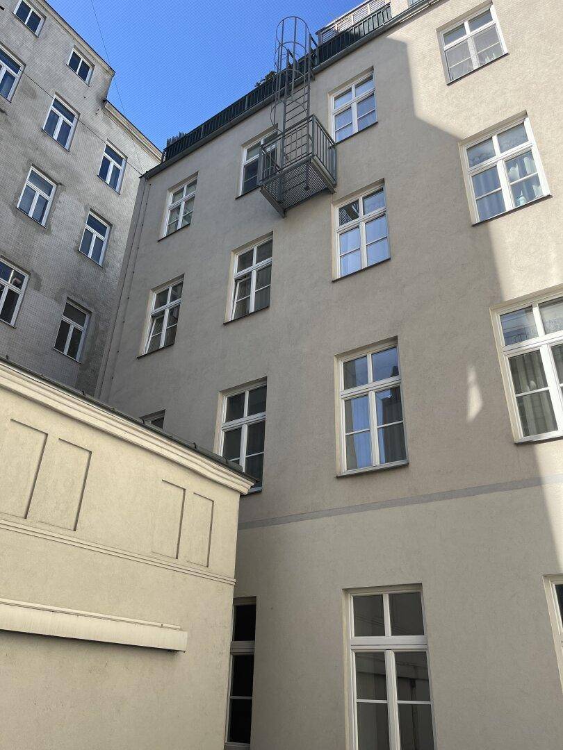 Fassade eines Gebäudes im Innenhof mit vielen Fenstern und einer Feuerleiter.