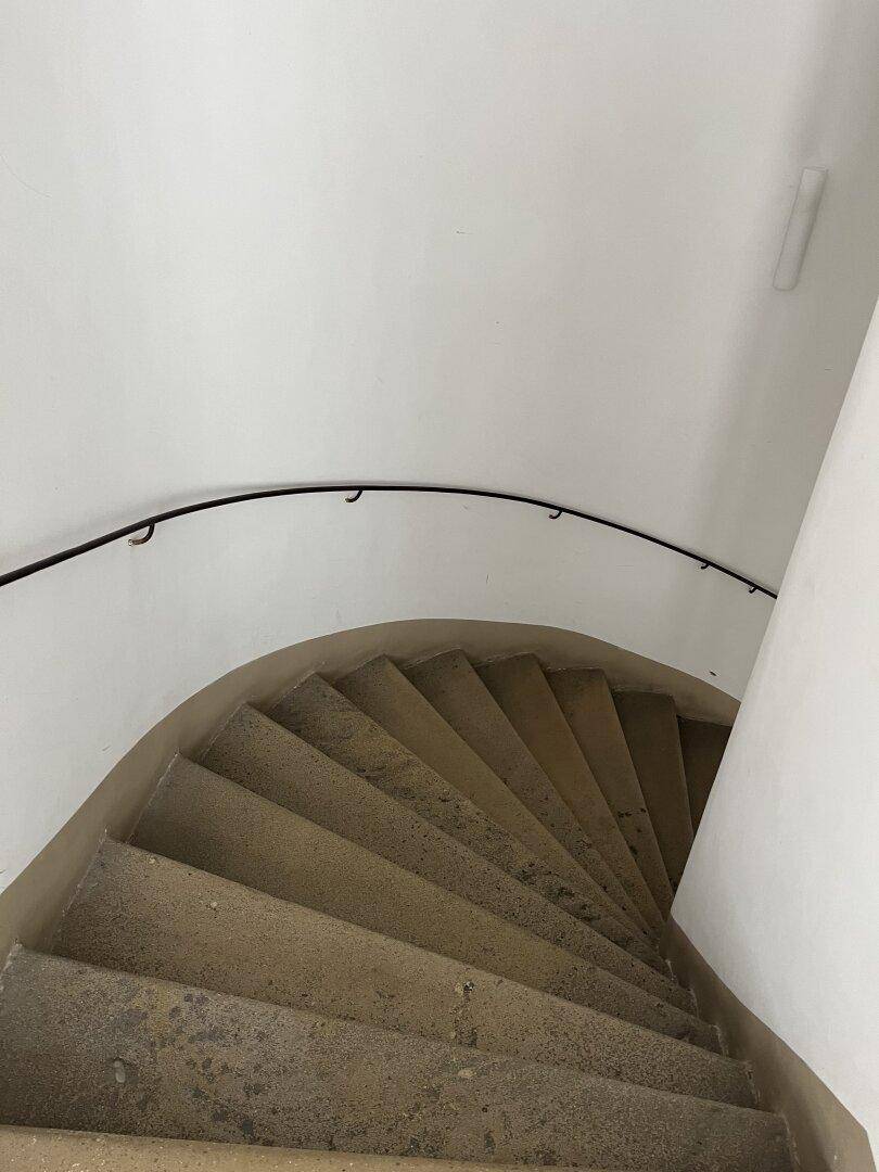 Geschwungene Steintreppe mit schlichtem Geländer, führt in die oberen Stockwerke des Gebäudes.