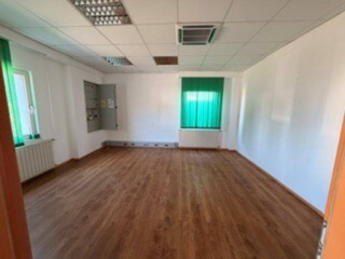 Geräumiges Büro mit zwei Fenstern, Heizkörpern und einem sichtbaren Elektroschaltkasten an der Wand.