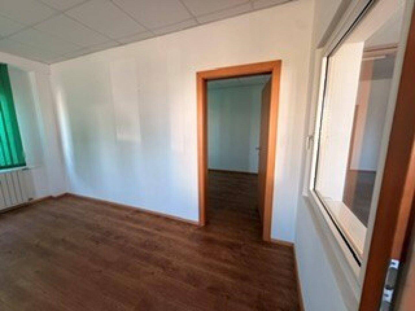Helles, leeres Büro mit Laminatboden, Heizkörper unter dem Fenster und weiß gestrichenen Wänden.