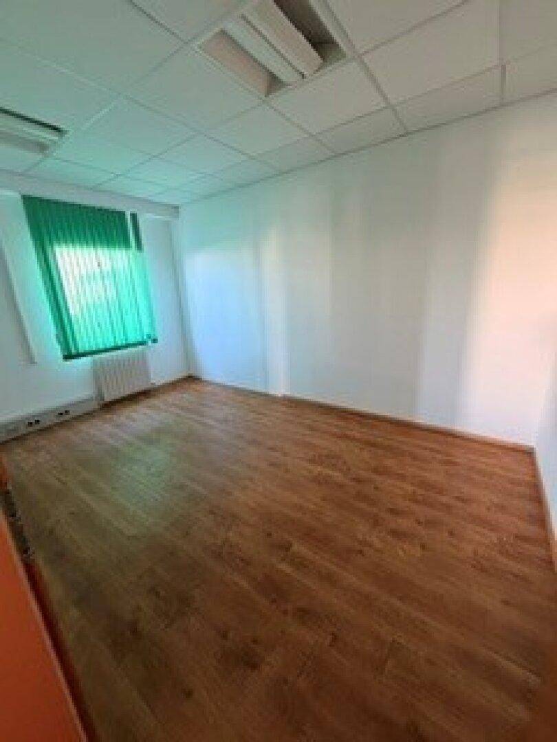 Leeres Büro mit Laminatboden und grünen Jalousien, die für Sichtschutz und Sonnenschutz sorgen.
