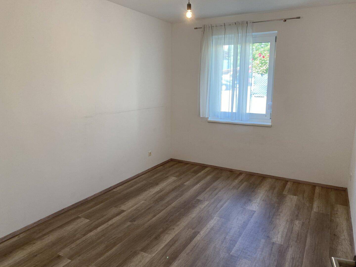 Helles Schlafzimmer mit Laminatboden und einem Fenster, bereit zur individuellen Gestaltung.