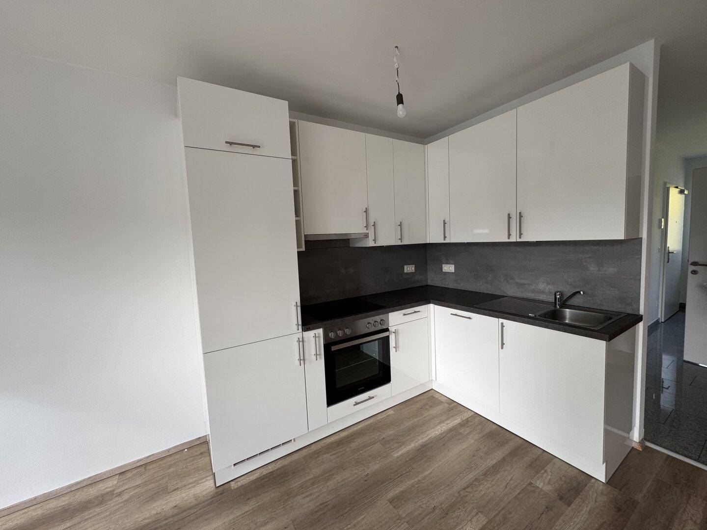Moderne, helle Einbauküche in L-Form mit weißen Hochglanzfronten und dunkler Arbeitsplatte.