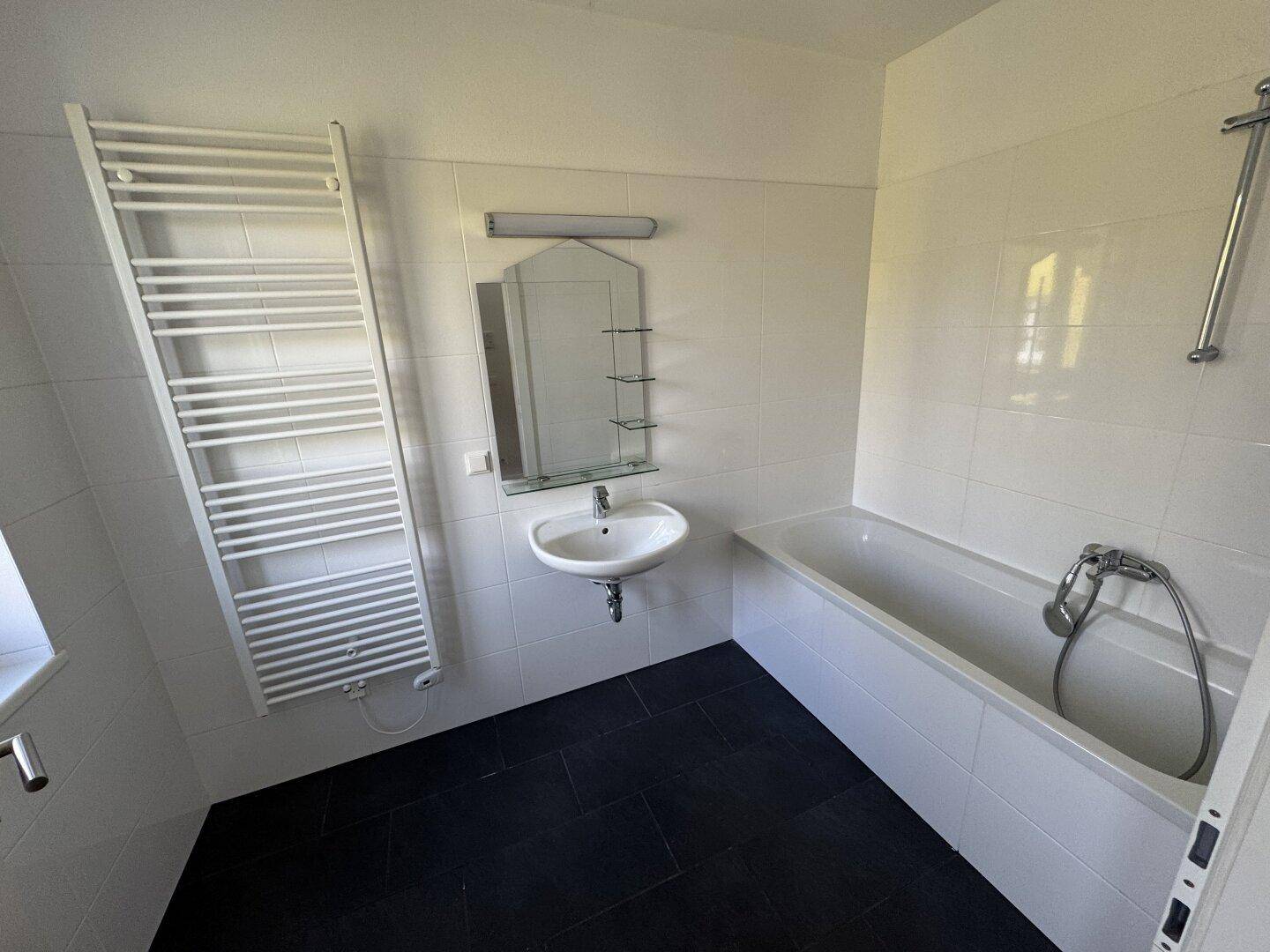 Funktionales Badezimmer mit Badewanne, Waschbecken, Spiegel und beheiztem Handtuchhalter.