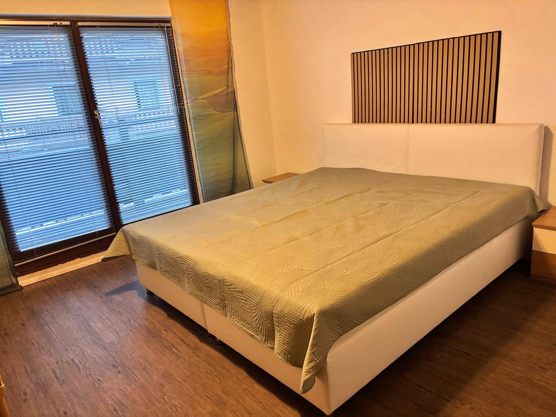 Gemütliches Schlafzimmer mit Doppelbett, Holzboden und Fenster mit Jalousien.