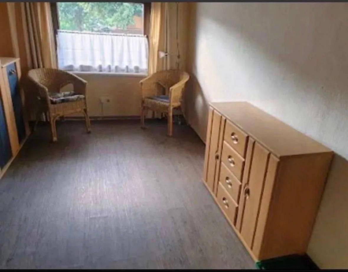 Heller Raum mit Laminatboden, zwei Korbsesseln am Fenster und einem Holzschrank.