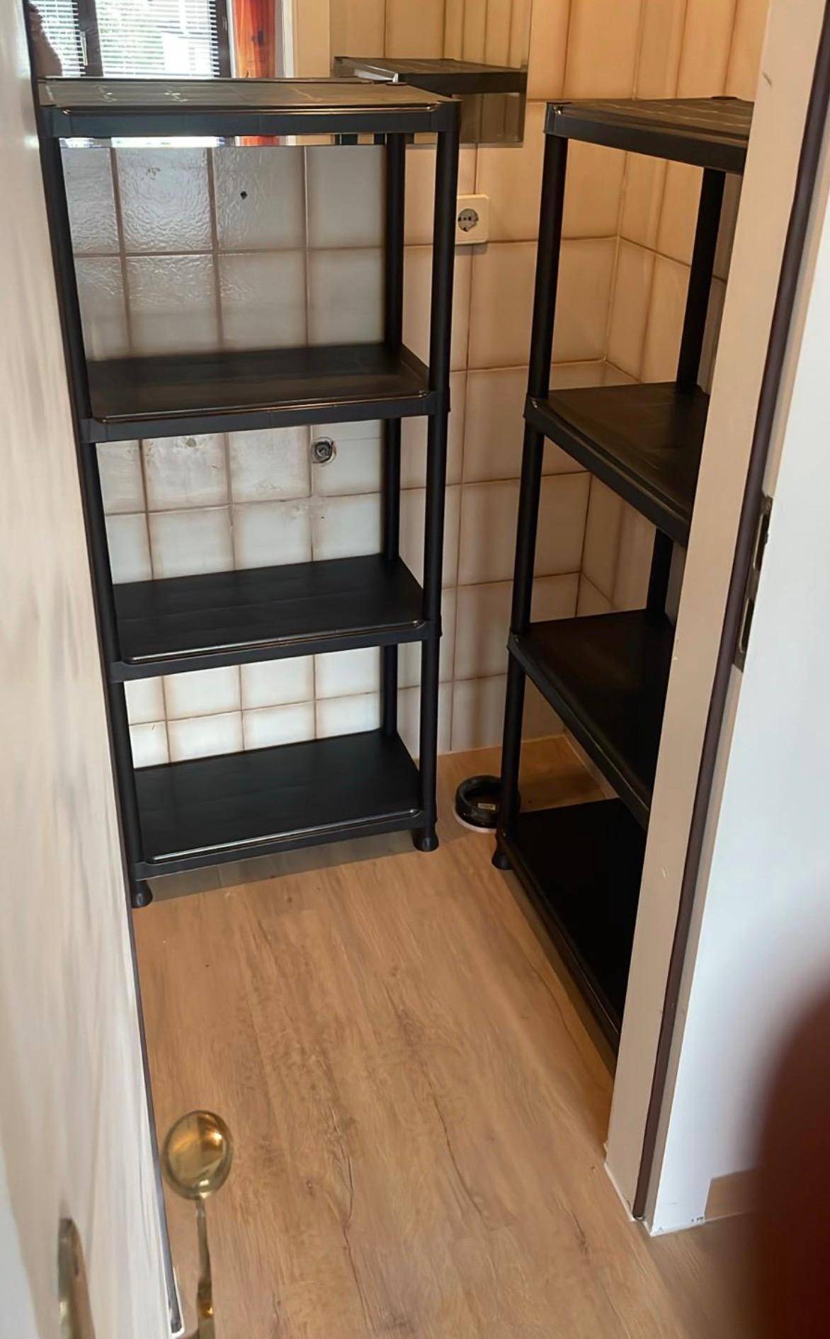 Funktionaler Abstellraum oder Hauswirtschaftsraum mit praktischen Regalen, hellen Wandfliesen und Laminatboden.