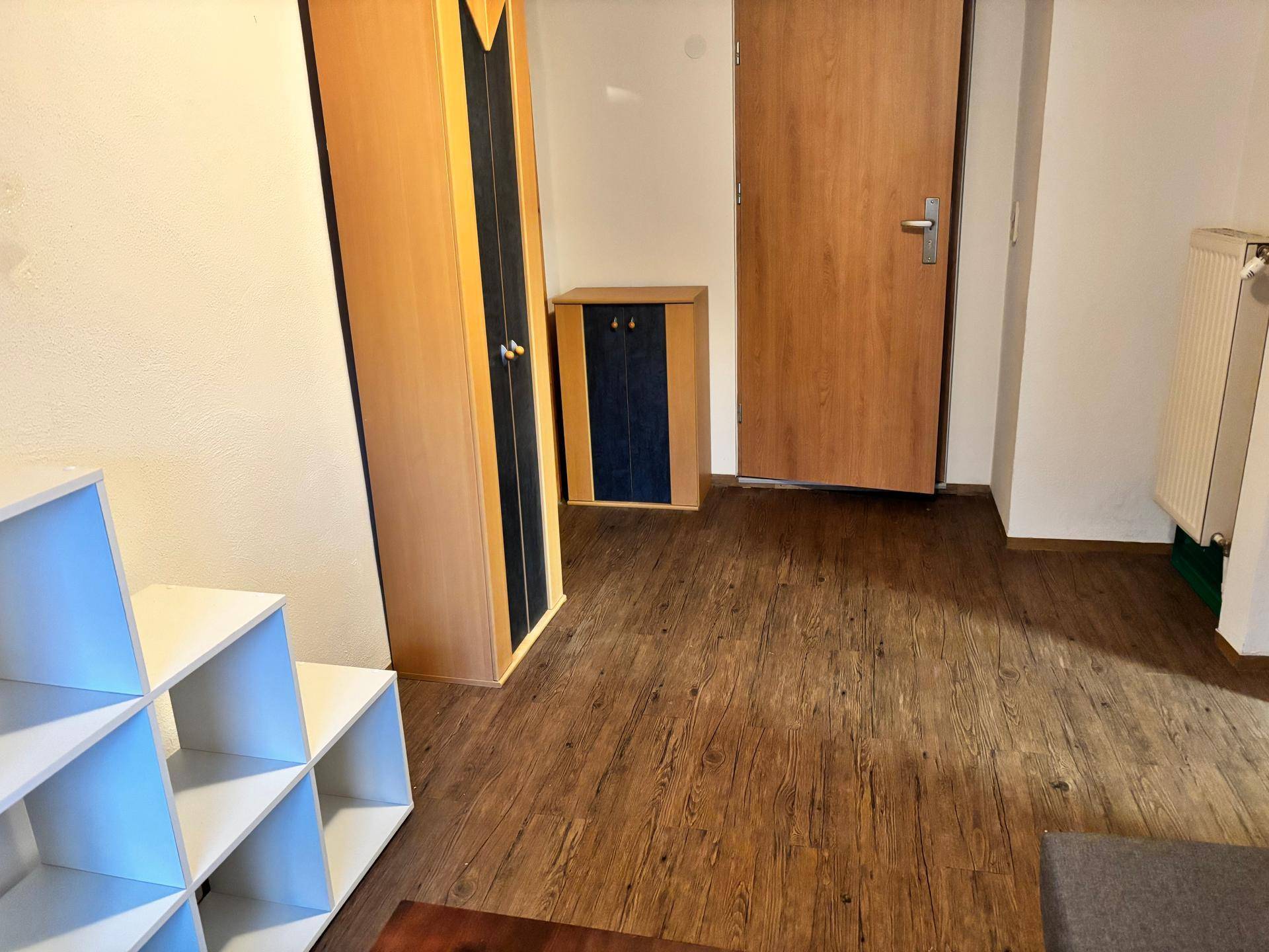 Flur mit Holzschrank, weißem Regal und Holzboden.