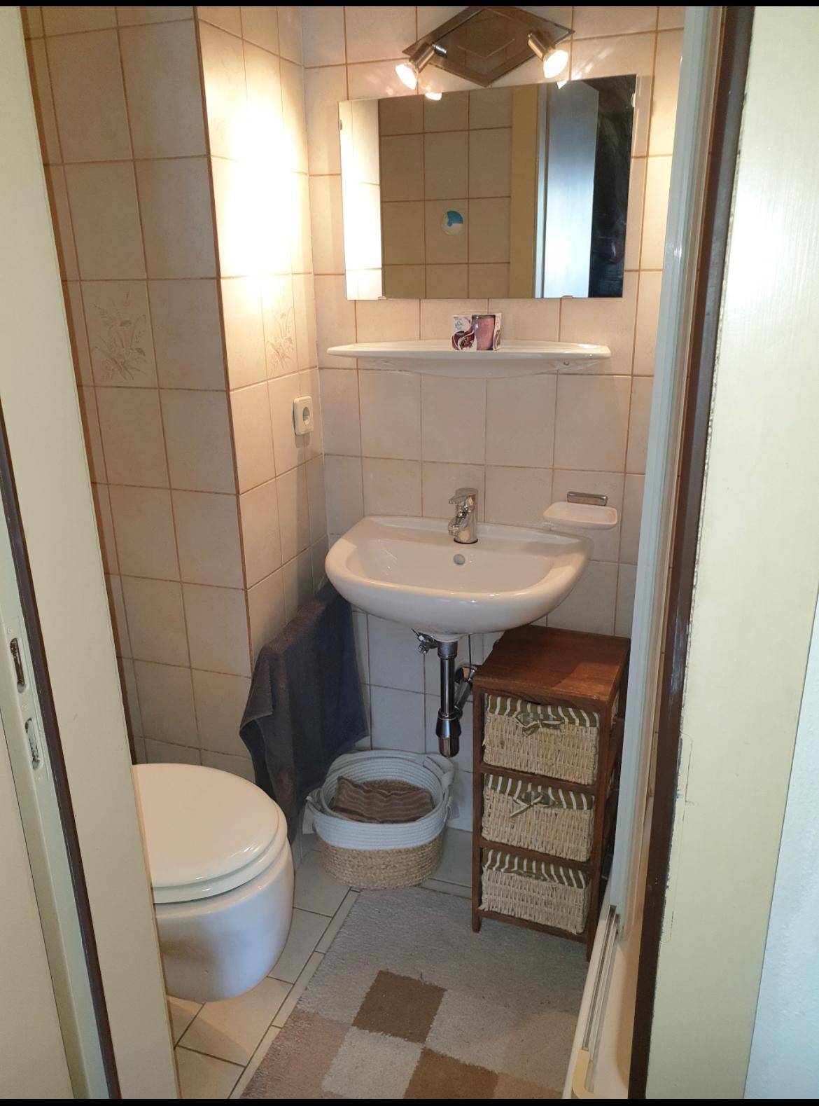 Kleines Gäste-WC mit beigefarbenen Fliesen, Waschbecken und Wand-WC.