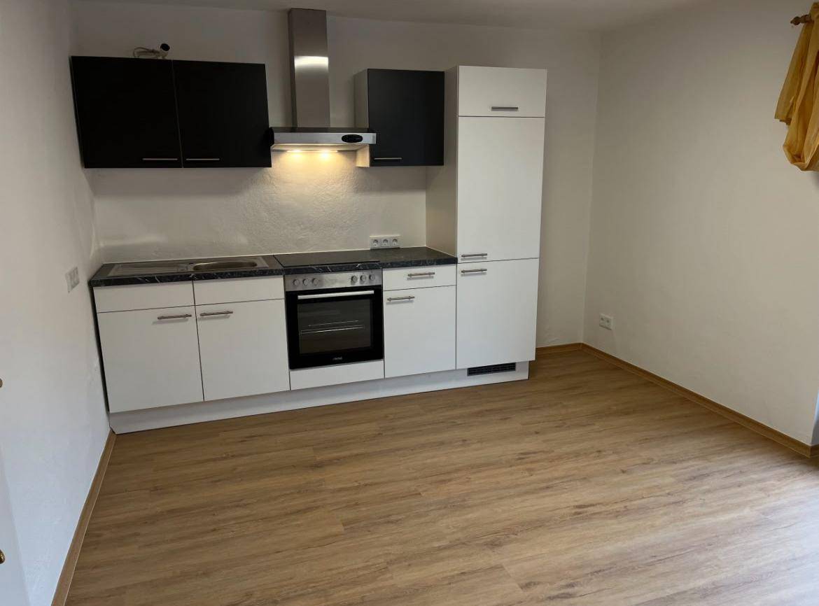 Moderne Küche mit weißen und schwarzen Schränken, Kochfeld und Dunstabzugshaube.