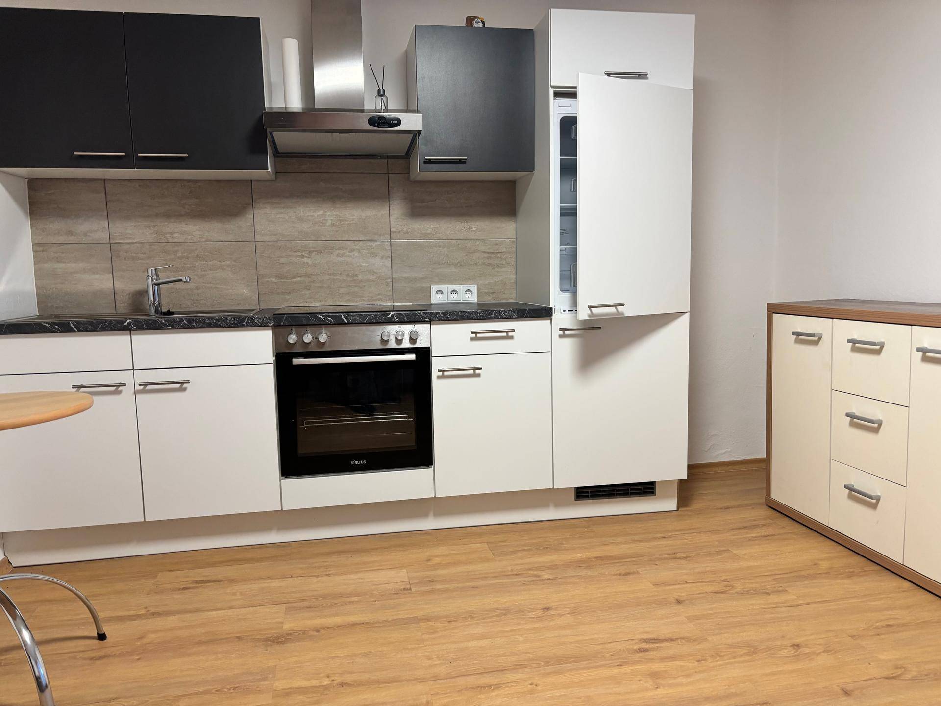 Moderne Einbauküche mit weißen und schwarzen Schränken, Backofen und Dunstabzugshaube.