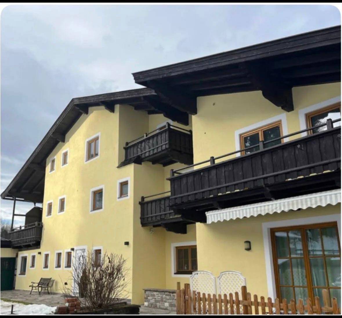 Gelbes Gebäude im alpinen Stil mit dunklen Holzbalkonen und Dachkonstruktion unter bewölktem Himmel.