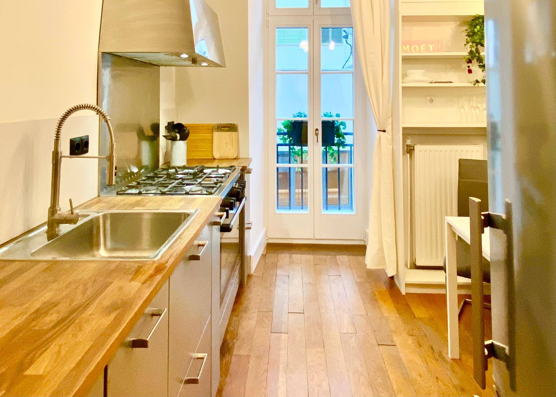 Moderne Küche mit Holzarbeitsplatte, Gasherd und Zugang zu einem französischen Balkon.