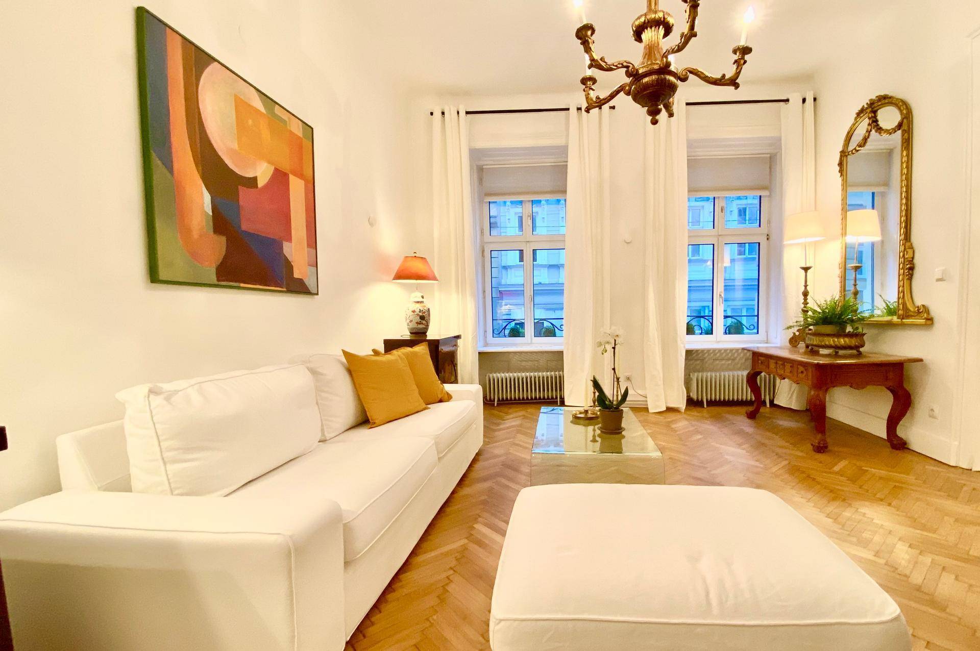 Helles Wohnzimmer mit Fischgrätparkett, eleganten Möbeln und einem Kronleuchter.