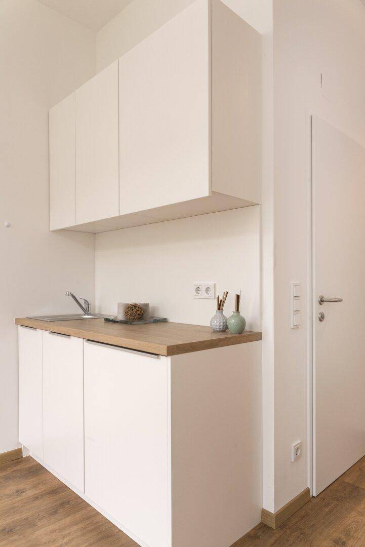 Kompakte Küchenzeile mit weißen Schränken, Holz-Arbeitsplatte und Spülbecken.