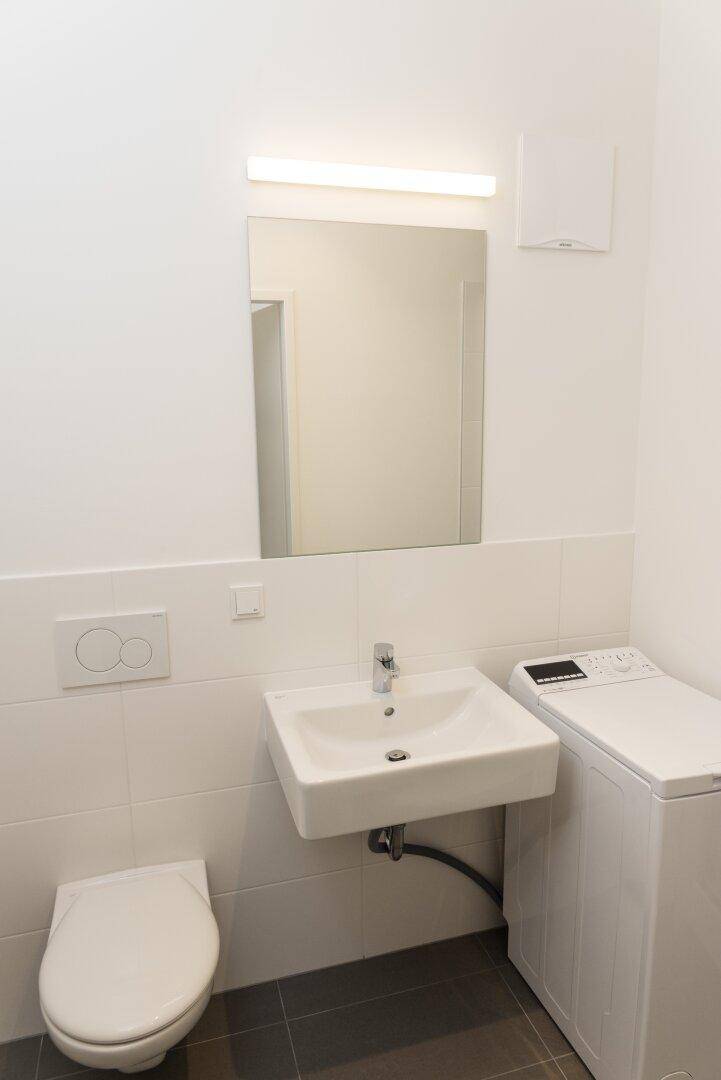 Modernes Badezimmer mit wandhängendem WC, Waschbecken und Waschmaschine.