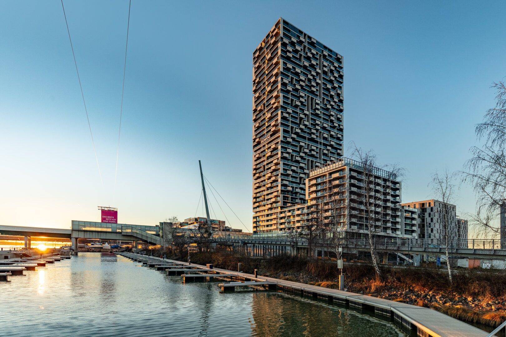Moderner Hochhauskomplex am Wasser mit Bootsanlegestellen bei Sonnenuntergang und weitem Blick.